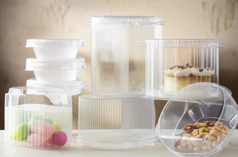 Diferentes tipos de embalagens transparentes para doces e bolos, mostrando variedade e design moderno em um ambiente de confeitaria